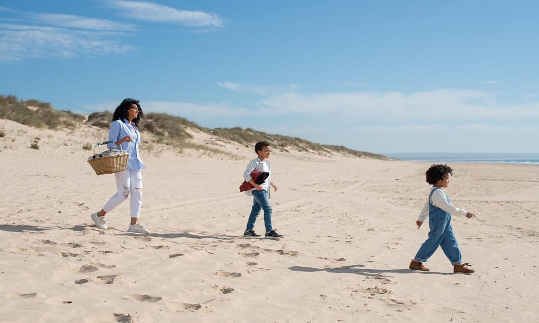 mãe e dois filhos a caminhar para fazer um piquenique na praia