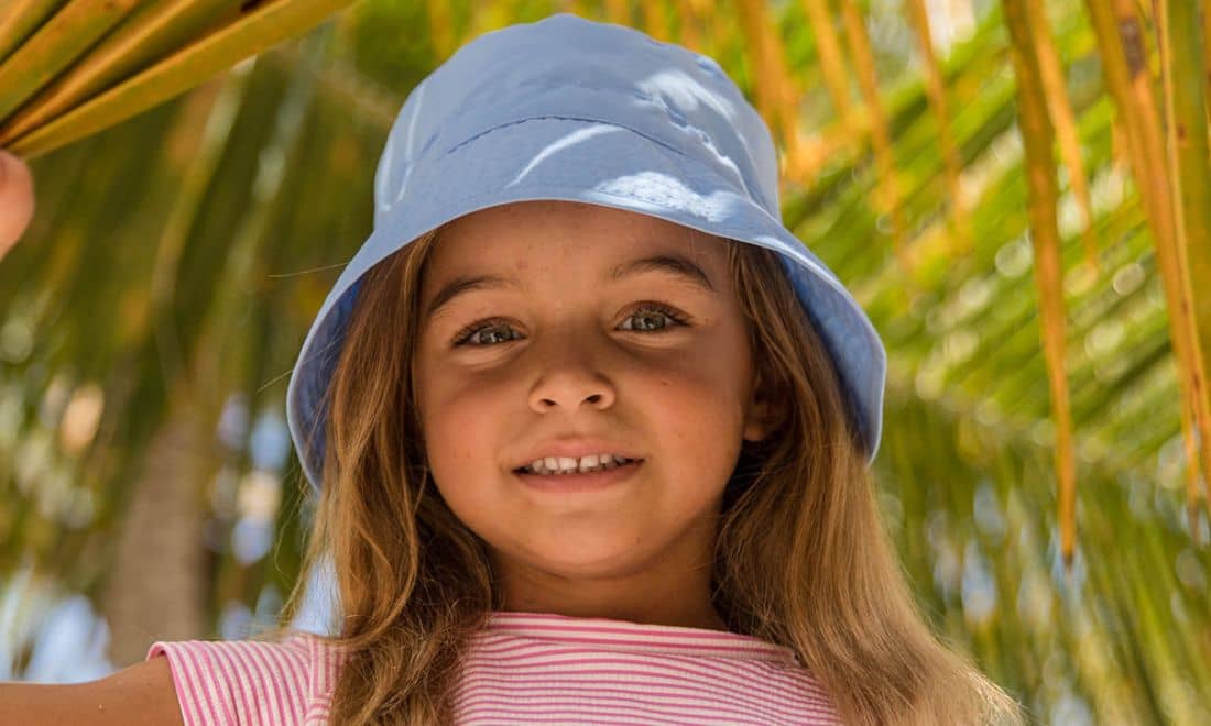 menina com chapéu azul e t-shirt cor-de-rosa debaixo de uma palmeira