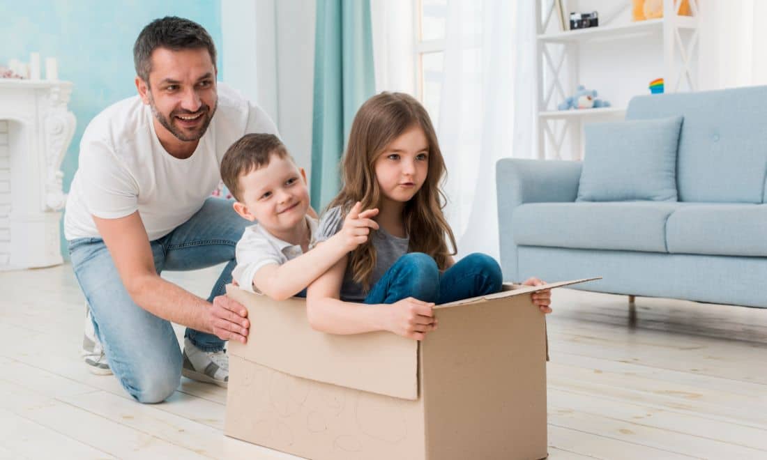 pai a empurrar caixa de cartão onde os dois filhos brincam juntos
