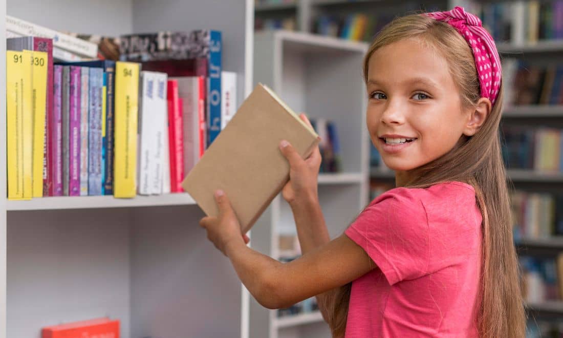 Manuais escolares Menina a colocar livro na estante livraria biblioteca