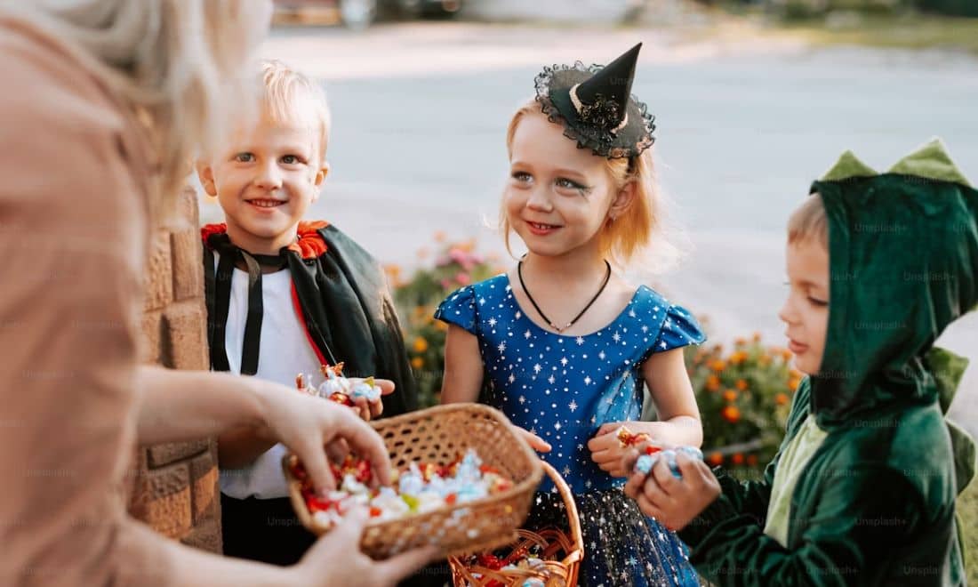 Halloween trick or treat crianças à porta doce ou travessura senhora com doces meninas bruxinha, menino vampiro e menino dinossauro