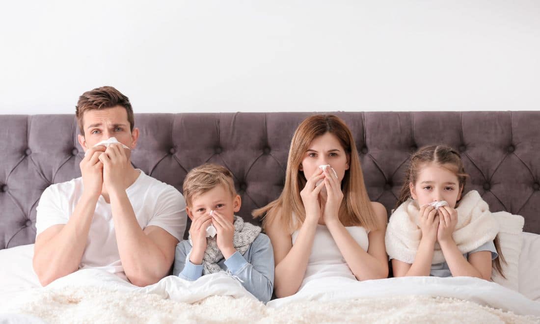 Gripe nas crianças família na cama mãe pai e filhos menina e menino com lenço no nariz doentes constipação