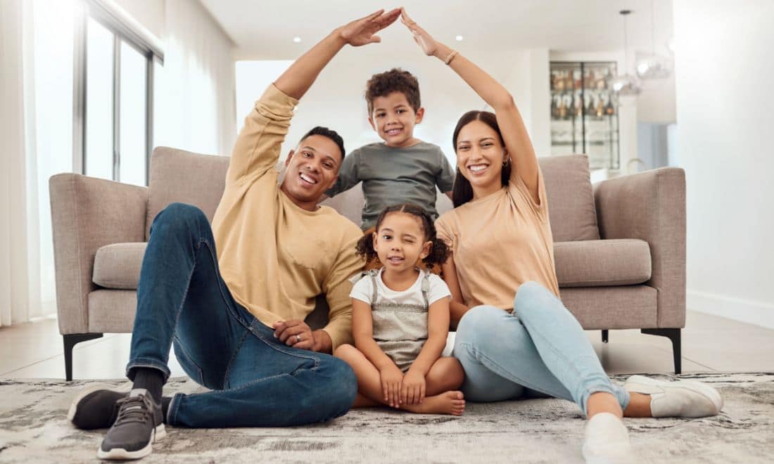 Família segurança casa pais a fazer casa em cima das crianças com os braços sentados no chão em frente ao sofá