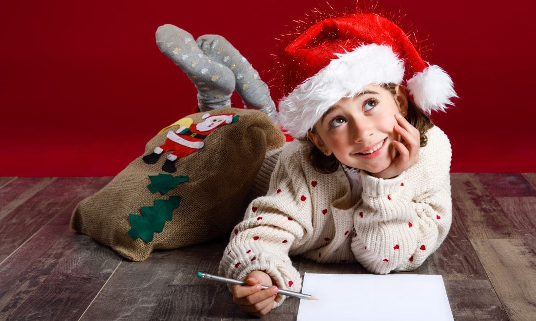 Menina no chão a escrever carta com chapéu de Pai Natal fundo vermelho geral