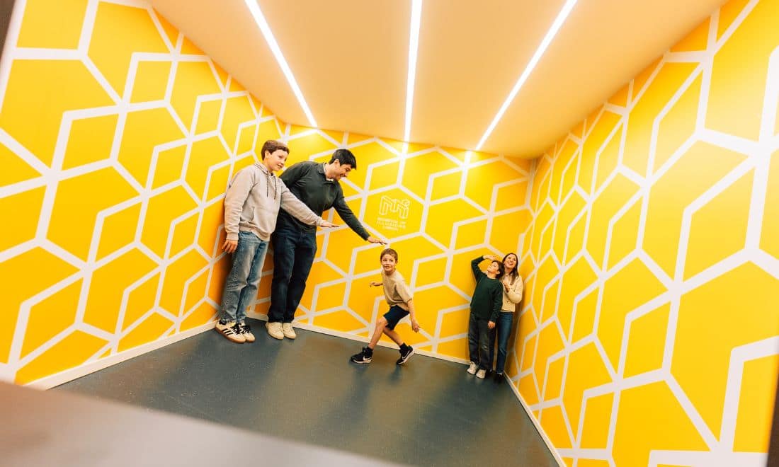 Museu das Ilusões família dentro de sala amarela com ilusão de tamanhos mais longe e mais perto