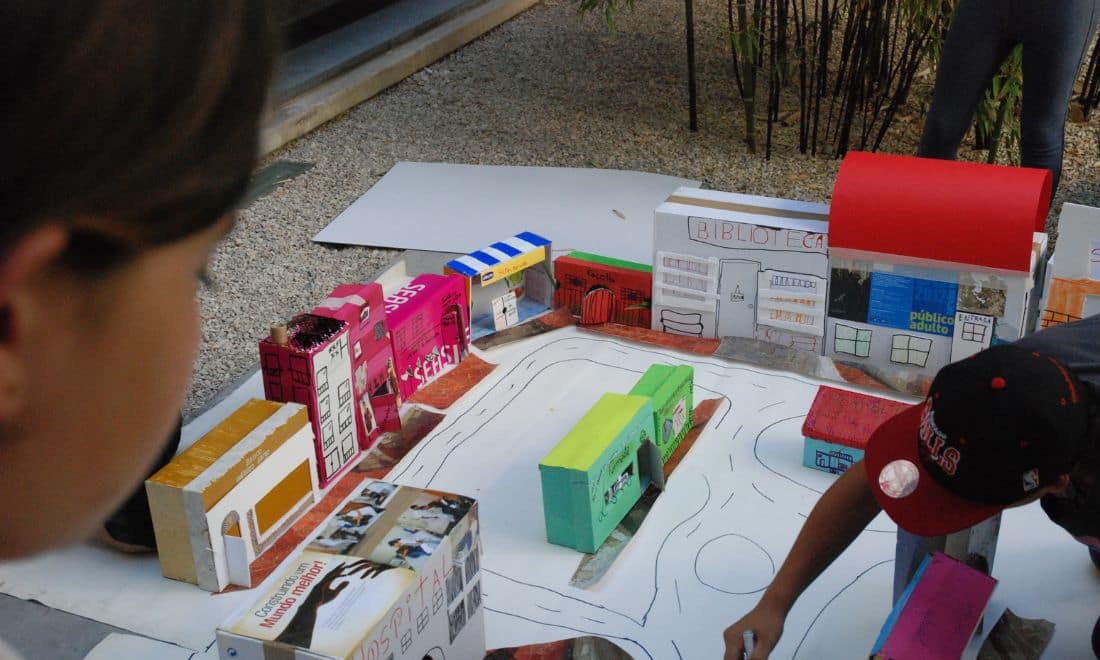 Cultura Santa Casa atividades para crianças e famílias em Lisboa Desenhar a Cidade edificios e cidade de papel e criança a olhar e outra de boné a montar peça