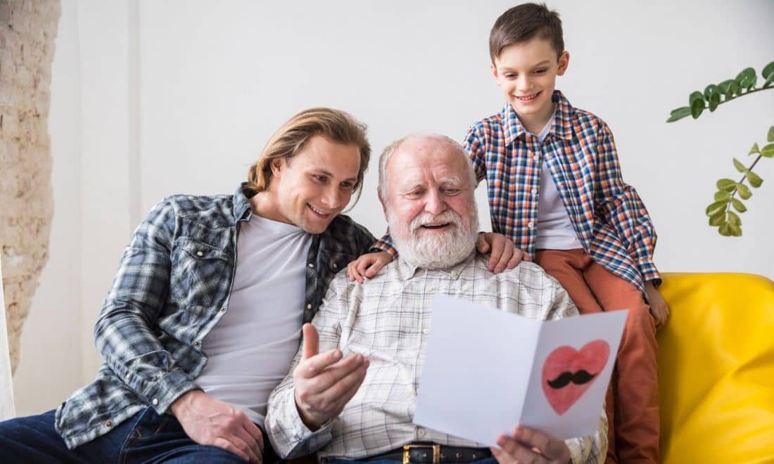 pai, filho e avô sentados no sofá a ler um postal